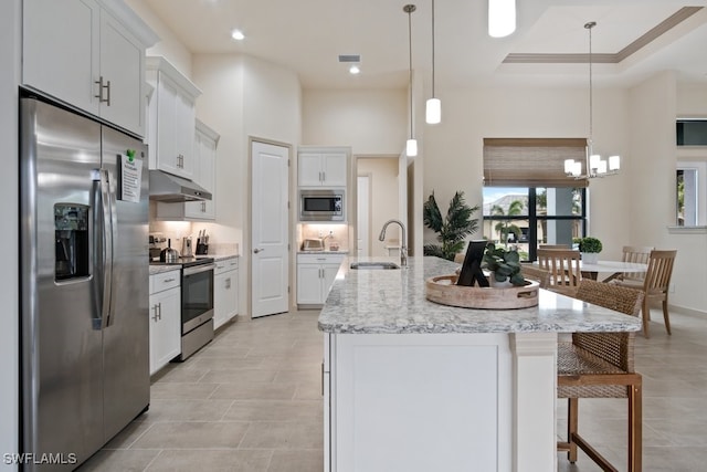 kitchen featuring sink, white cabinetry, stainless steel appliances, a center island with sink, and decorative light fixtures