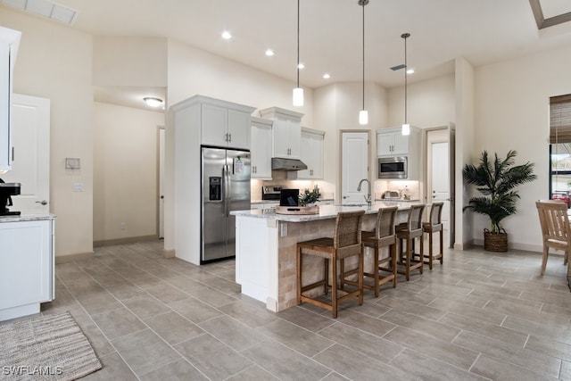 kitchen with white cabinetry, light stone counters, appliances with stainless steel finishes, pendant lighting, and a high ceiling