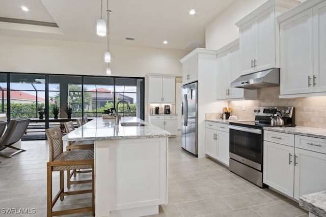 kitchen featuring sink, light stone counters, hanging light fixtures, stainless steel appliances, and a kitchen island with sink