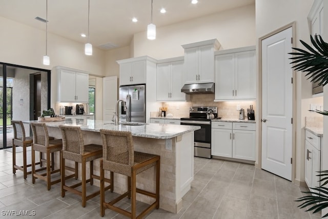 kitchen with stainless steel appliances, white cabinetry, a center island with sink, and light stone counters