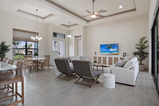 living room with a raised ceiling, a high ceiling, and ceiling fan with notable chandelier