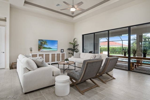 living room featuring a raised ceiling, a high ceiling, and ceiling fan