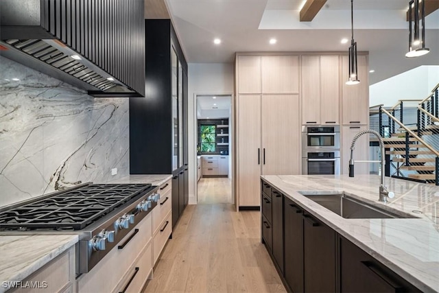 kitchen featuring light stone countertops, decorative light fixtures, stainless steel appliances, custom range hood, and sink