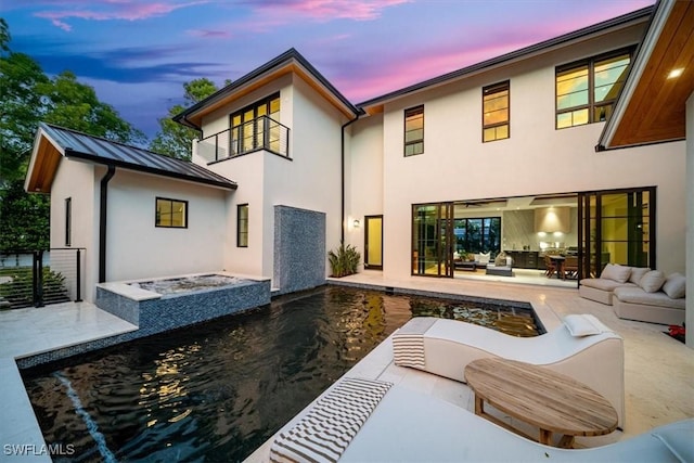 back house at dusk featuring a pool, an outdoor living space with a fire pit, and a patio