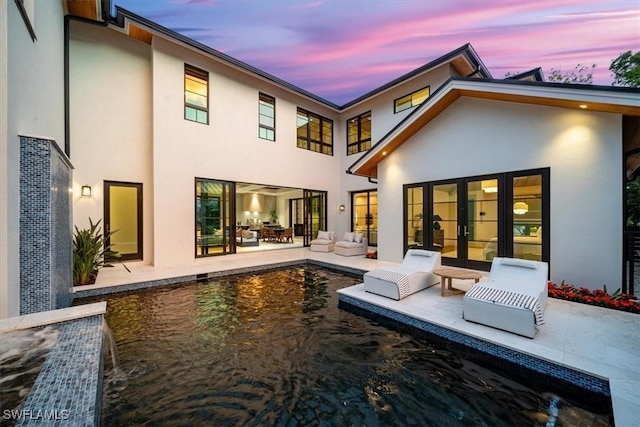 back house at dusk featuring french doors and a patio area