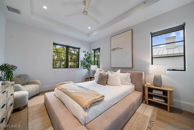 bedroom featuring ceiling fan, light hardwood / wood-style flooring, and a tray ceiling