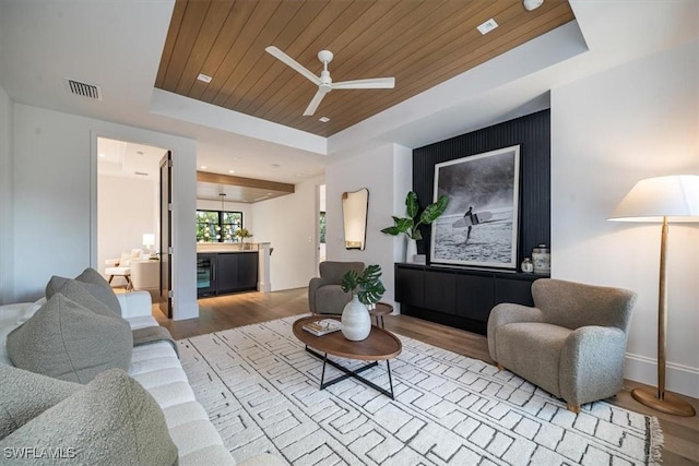 living room featuring wooden ceiling, a raised ceiling, wine cooler, light hardwood / wood-style floors, and ceiling fan