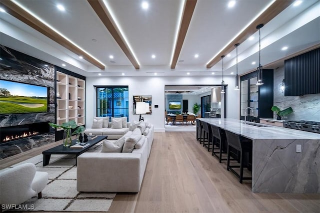 living room featuring sink, beamed ceiling, built in features, light hardwood / wood-style flooring, and a high end fireplace