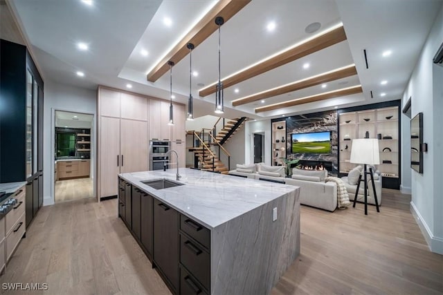 kitchen featuring a large fireplace, light hardwood / wood-style floors, hanging light fixtures, a large island with sink, and light stone counters