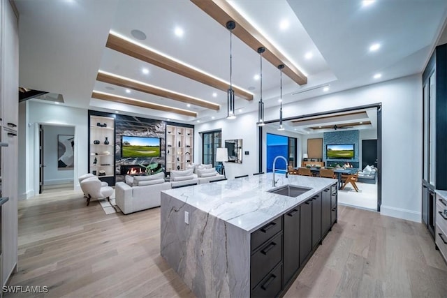 kitchen with hanging light fixtures, light wood-type flooring, a large island with sink, light stone countertops, and sink