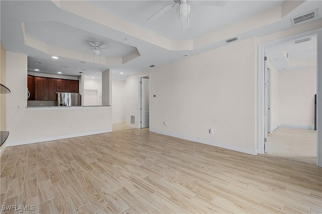 unfurnished living room featuring a raised ceiling, ceiling fan, and light wood-type flooring