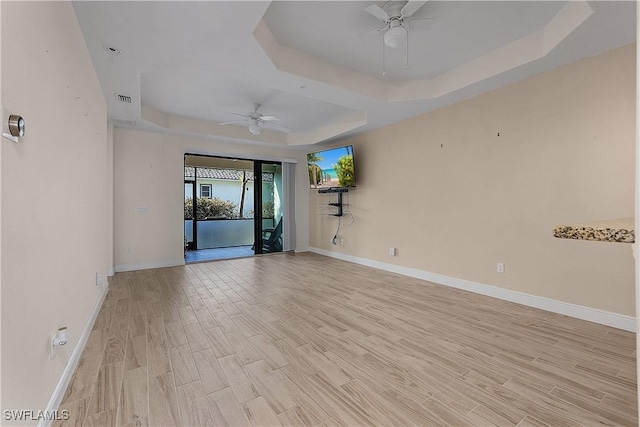 spare room with ceiling fan, light wood-type flooring, and a raised ceiling