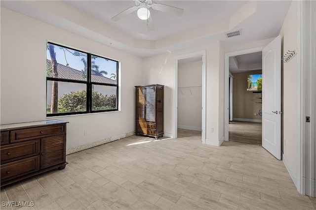 bedroom with a closet, a raised ceiling, light hardwood / wood-style floors, ceiling fan, and a walk in closet