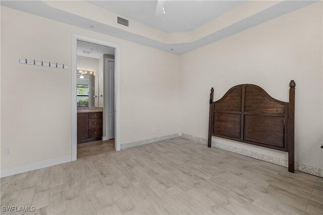 unfurnished bedroom with ceiling fan, light wood-type flooring, connected bathroom, and a raised ceiling