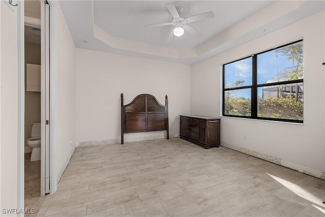 unfurnished bedroom featuring ceiling fan, a tray ceiling, and connected bathroom