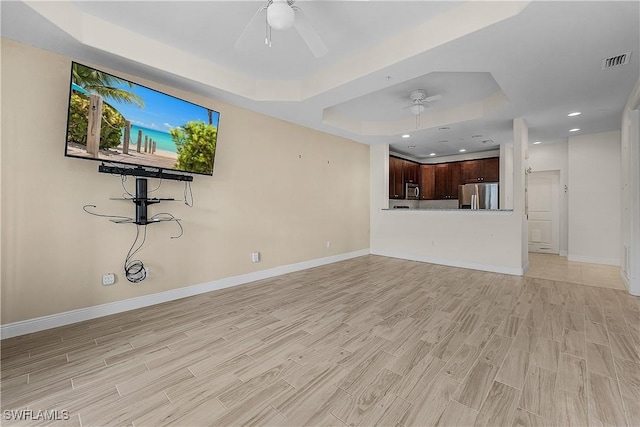 unfurnished living room with ceiling fan and a tray ceiling