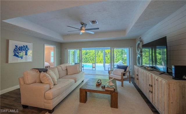 living room with a tray ceiling, ceiling fan, wooden walls, and hardwood / wood-style flooring