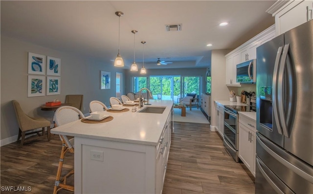 kitchen featuring ceiling fan, decorative light fixtures, a center island with sink, white cabinets, and appliances with stainless steel finishes