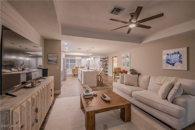 living room with a tray ceiling, ceiling fan, sink, and light hardwood / wood-style floors