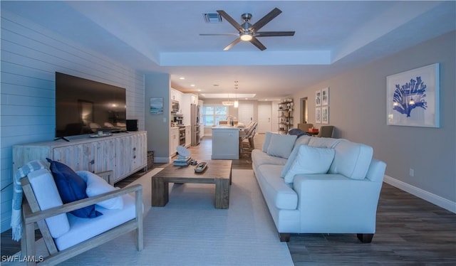 living room featuring hardwood / wood-style floors, a raised ceiling, and ceiling fan