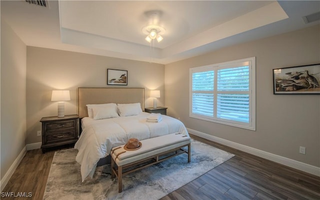 bedroom with a tray ceiling, ceiling fan, and dark wood-type flooring