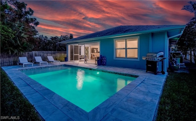 pool at dusk with area for grilling and a patio