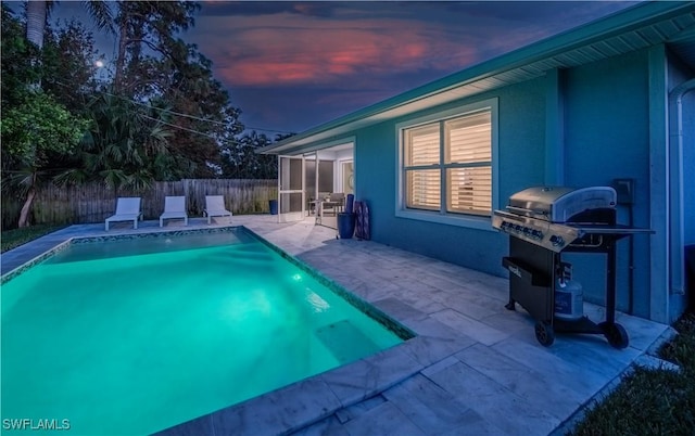 pool at dusk featuring a sunroom, a grill, and a patio area