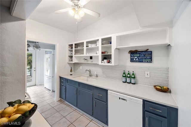 kitchen with white appliances, blue cabinets, vaulted ceiling, sink, and light tile patterned floors