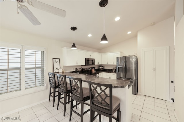 kitchen featuring stainless steel fridge, white cabinets, dark countertops, a kitchen breakfast bar, and a peninsula