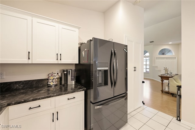 kitchen featuring light tile patterned floors, baseboards, white cabinets, stainless steel refrigerator with ice dispenser, and dark stone countertops