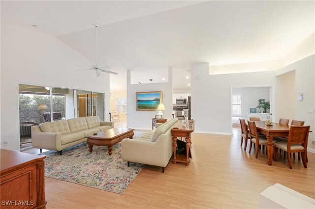 living area featuring high vaulted ceiling, light wood-style flooring, and baseboards