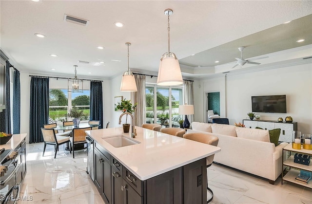 kitchen featuring ceiling fan with notable chandelier, crown molding, sink, hanging light fixtures, and an island with sink