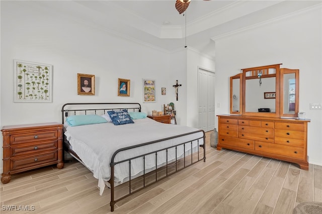 bedroom featuring ornamental molding, a tray ceiling, ceiling fan, light hardwood / wood-style flooring, and a closet