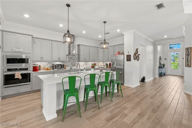 kitchen featuring gray cabinetry, decorative backsplash, a kitchen bar, a kitchen island with sink, and appliances with stainless steel finishes