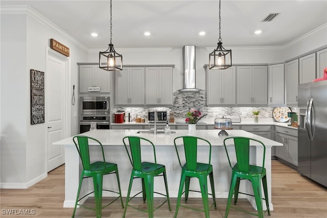 kitchen with a center island with sink, wall chimney range hood, and appliances with stainless steel finishes