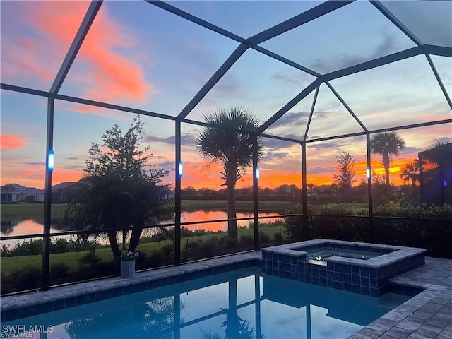 pool at dusk with an in ground hot tub, a water view, and glass enclosure