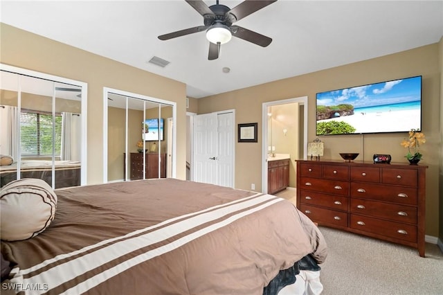 carpeted bedroom with two closets, ensuite bathroom, and ceiling fan