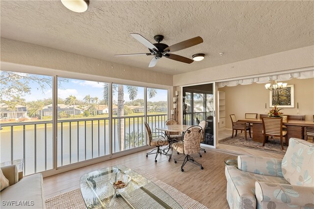 sunroom / solarium with ceiling fan with notable chandelier and a water view