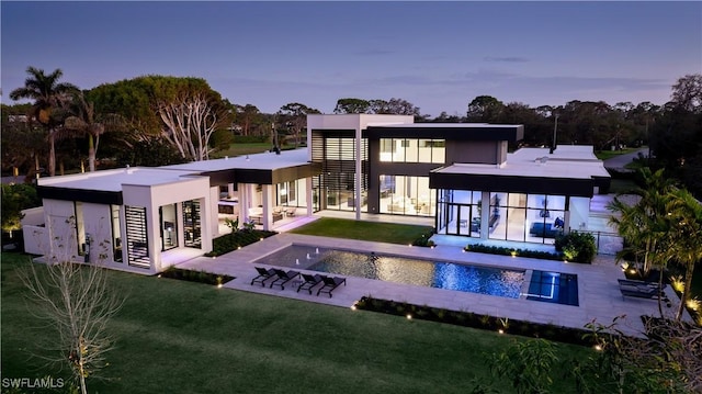 back of house at dusk featuring a patio area, a lawn, and an outdoor pool