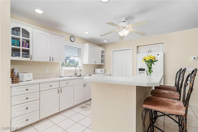 kitchen with sink, white cabinets, a kitchen breakfast bar, and white appliances