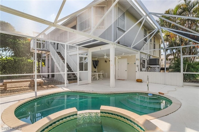 rear view of property featuring a lanai, a swimming pool with hot tub, and a patio area