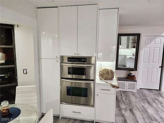 kitchen with stainless steel double oven, light hardwood / wood-style floors, and white cabinetry