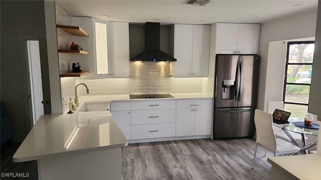 kitchen with wall chimney exhaust hood, stainless steel fridge, decorative backsplash, white cabinetry, and sink