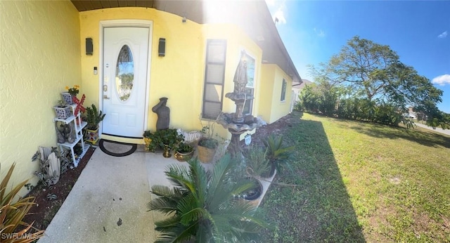 view of exterior entry with a yard and stucco siding