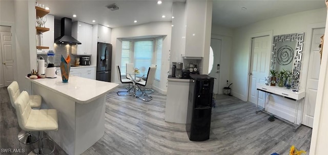 kitchen with wall chimney exhaust hood, black fridge, light wood-style floors, white cabinetry, and backsplash