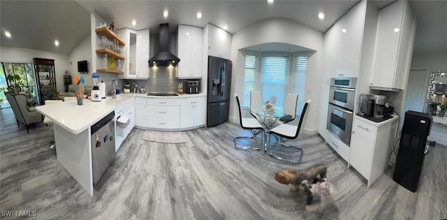 kitchen featuring a peninsula, white cabinetry, appliances with stainless steel finishes, wall chimney range hood, and modern cabinets