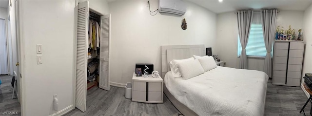 bedroom featuring a closet, a wall unit AC, baseboards, and wood finished floors