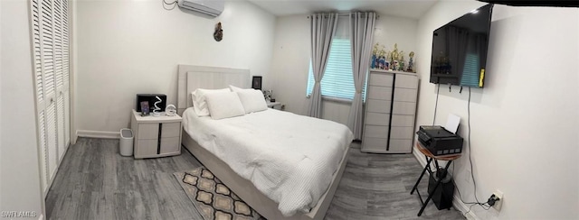 bedroom featuring wood finished floors, baseboards, and a wall mounted AC