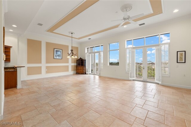 empty room with ceiling fan with notable chandelier, a wealth of natural light, and a raised ceiling