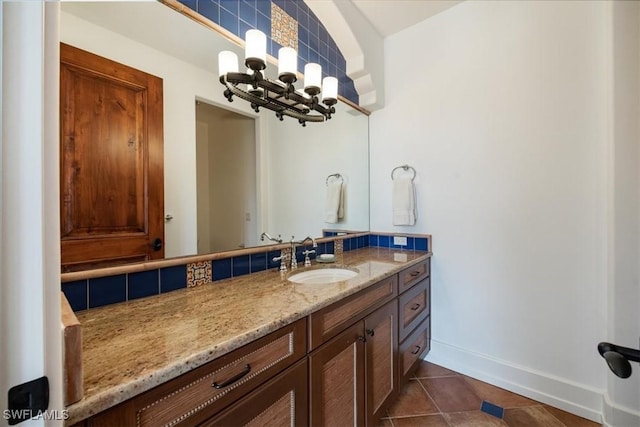 bathroom featuring a notable chandelier, backsplash, vanity, baseboards, and tile patterned floors